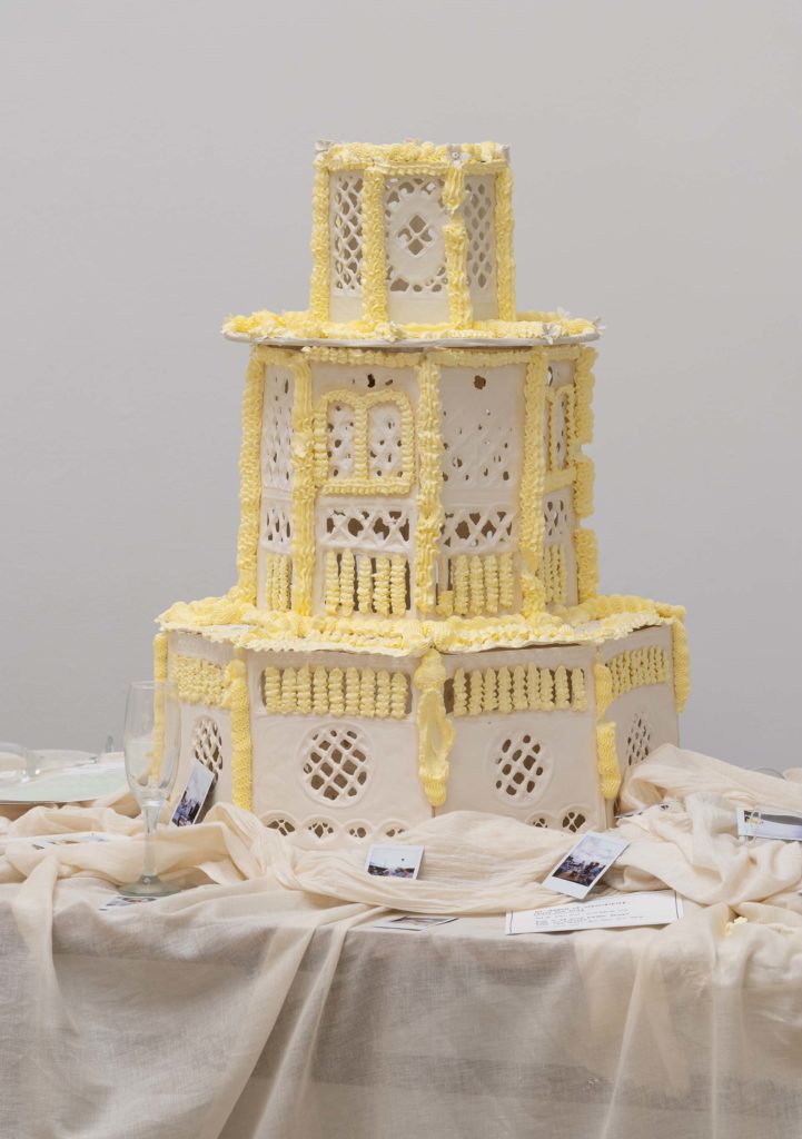 A wedding cake, surrounded by a draped tablecloth and polaroid photos.